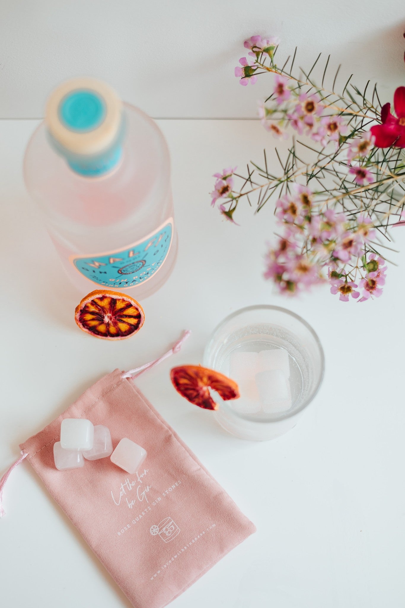 Rose Quartz Gin Stones with pouch; a glass and bottle of pink gin 